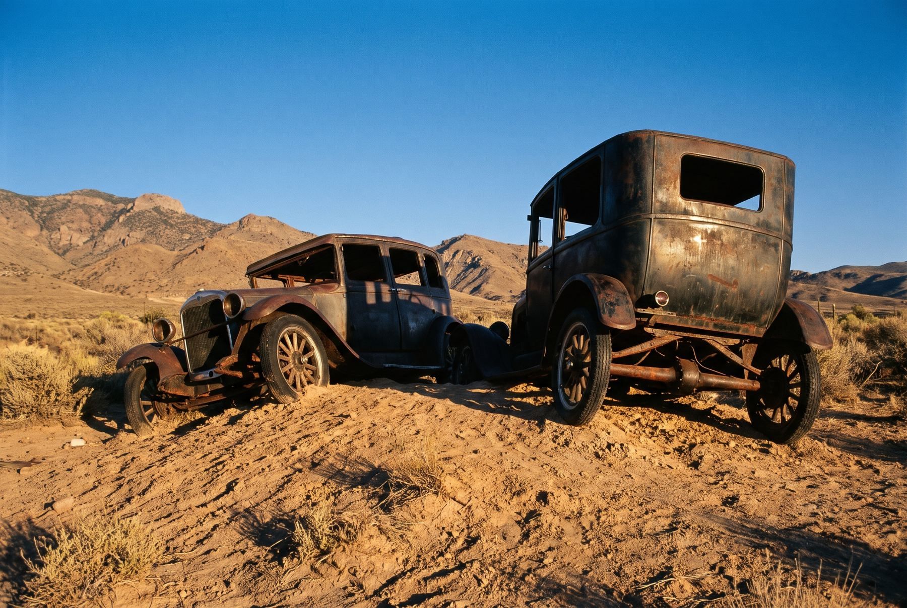 Two vintage automobiles standing upright nose-first in Nevada desert gravel.