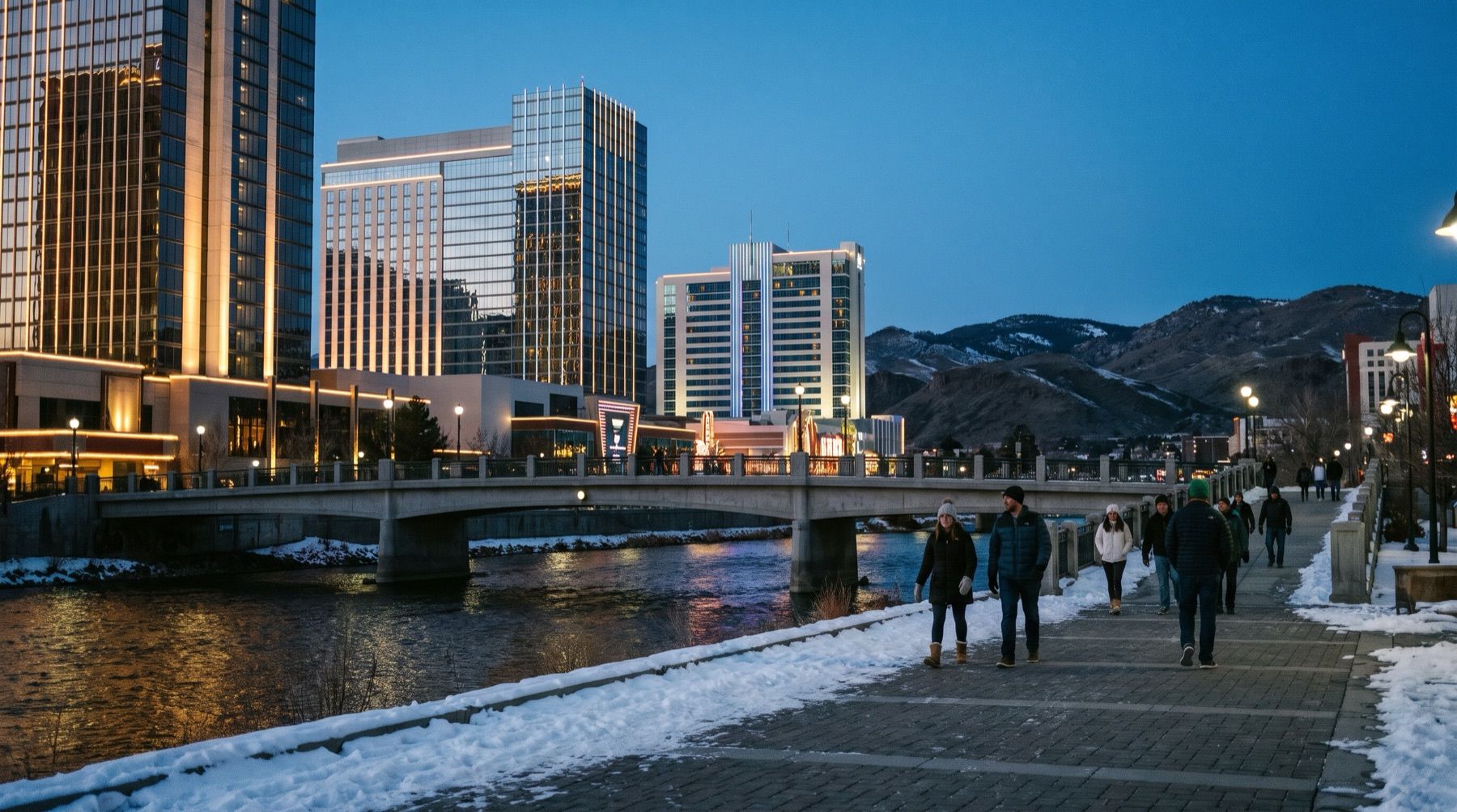 Lit casino-hotel towers above the Truckee River walk in downtown Reno at dusk in winter, snow on the hills behind